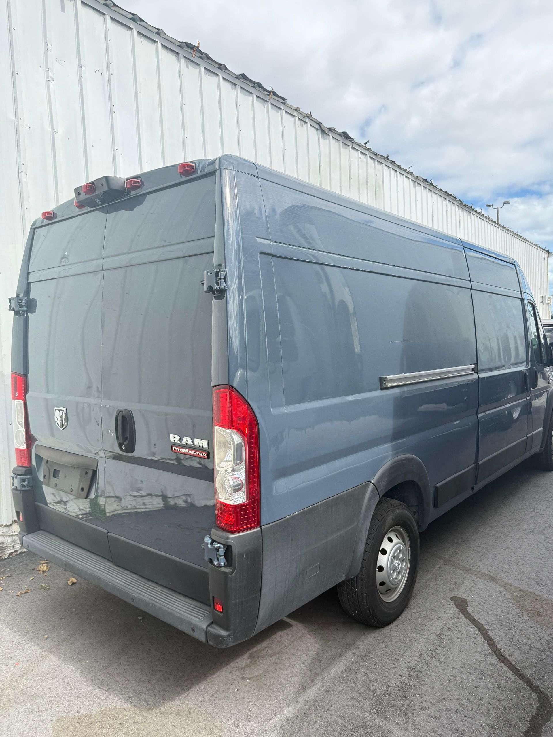 Gray Ram ProMaster van parked outside, against a white building.