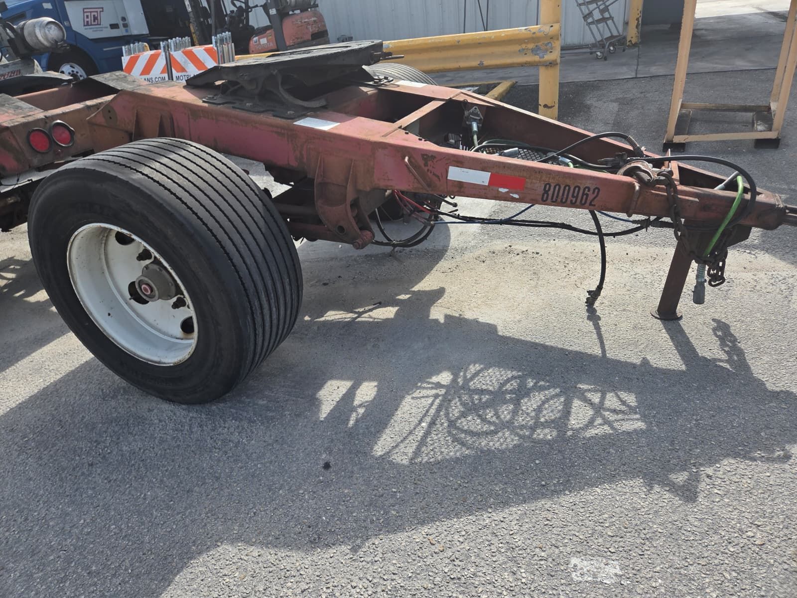 Red commercial semi-trailer chassis with a tire, a hitch, and a shadow cast on asphalt.