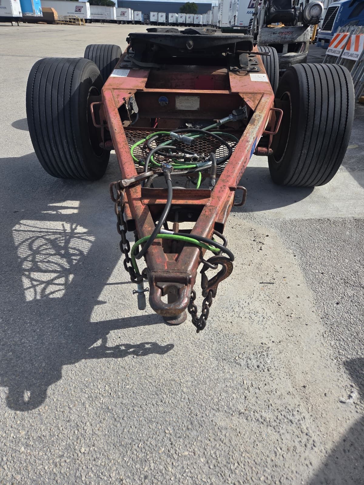 Red gooseneck trailer with black tires, chains, and electrical wiring, parked on asphalt.