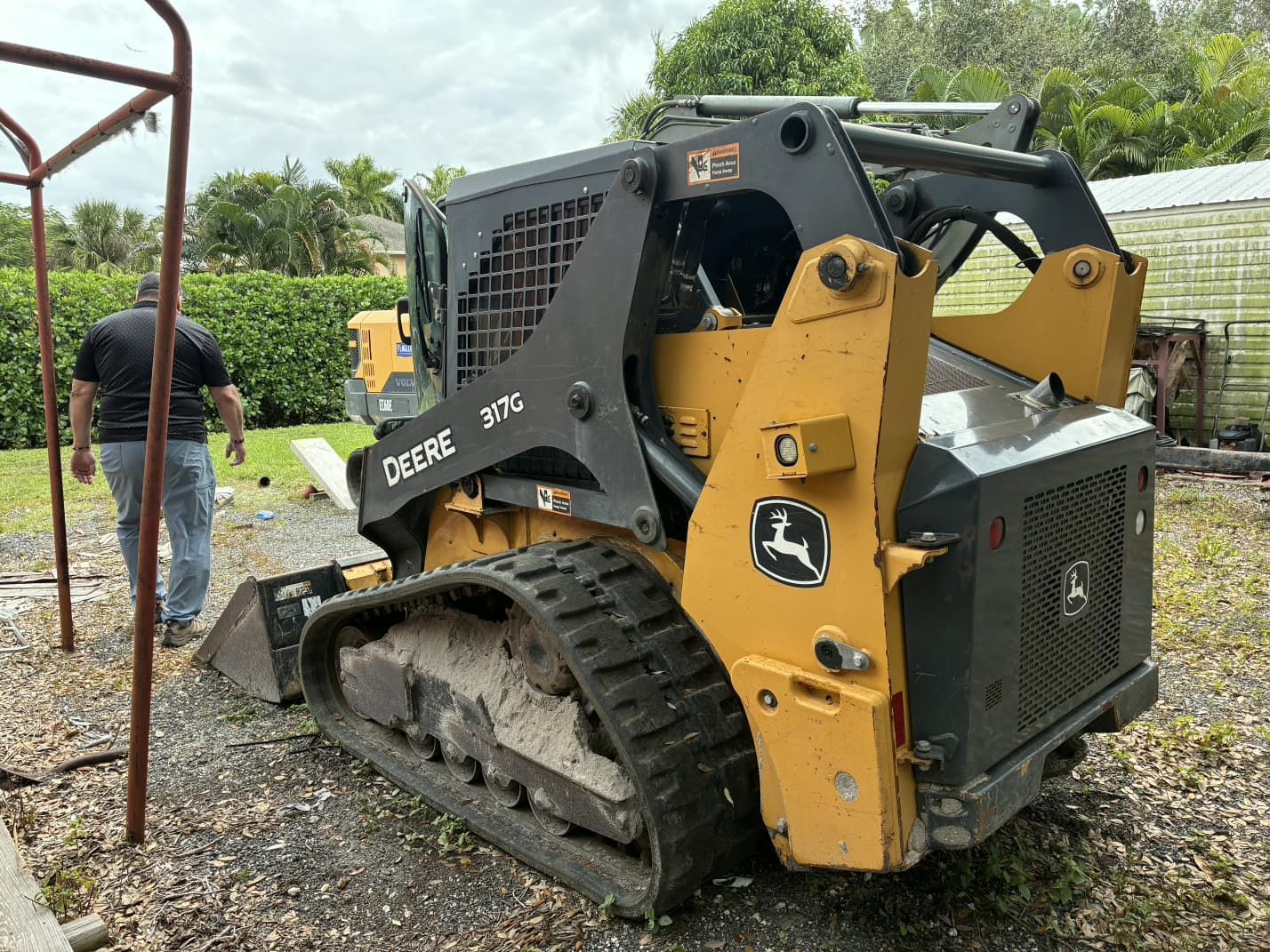 John Deere skid steer loader in a yard; a person walks away from it.