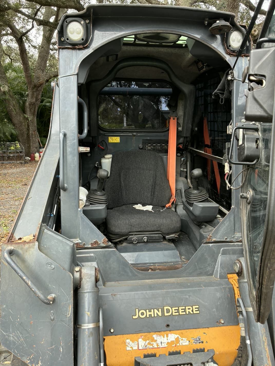 Inside view of a John Deere skid steer loader with an open cab and worn seat.
