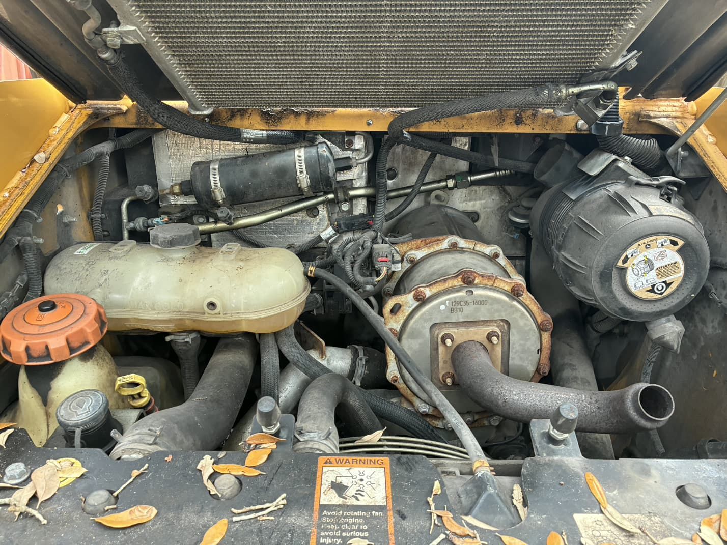 Engine compartment of a yellow construction machine with various components including a coolant reservoir, and a radiator.