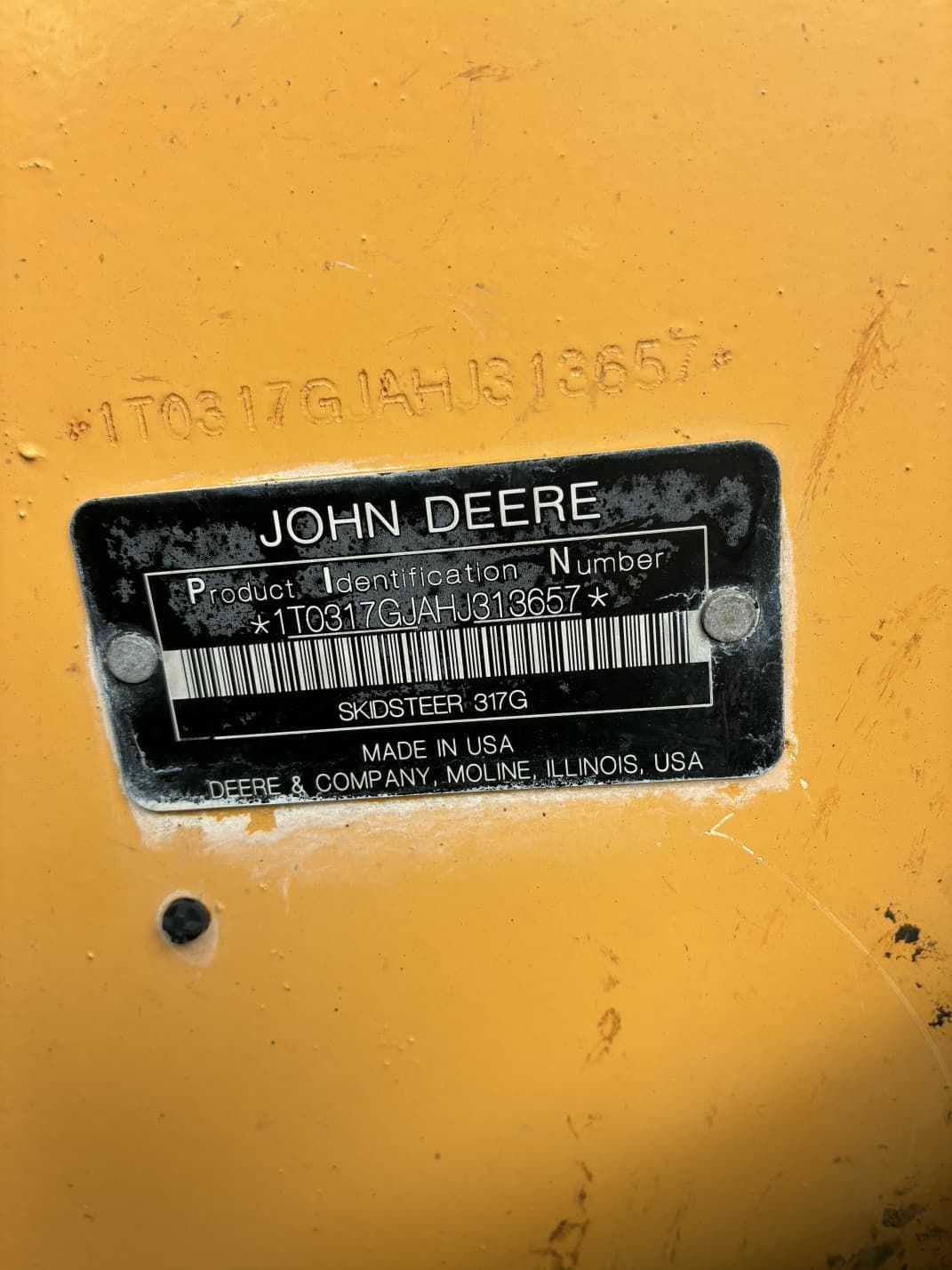 John Deere equipment identification plate, black on yellow background, showing serial number and manufacturing details.