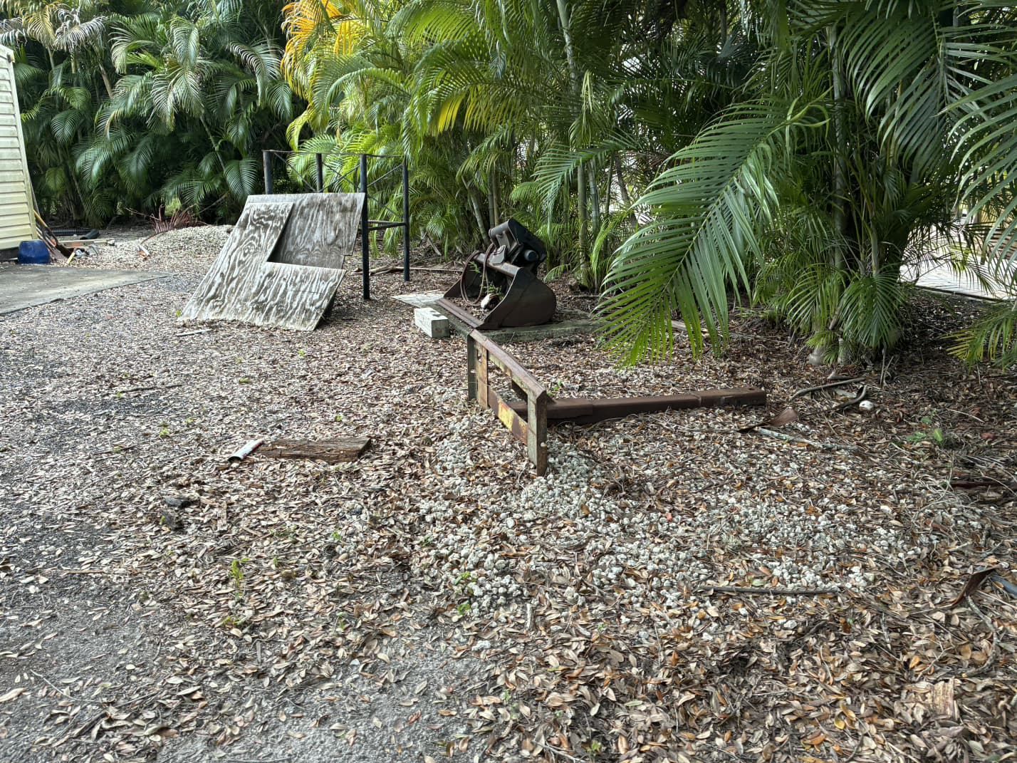 Debris-covered ground with pieces of metal and concrete, foliage in background.