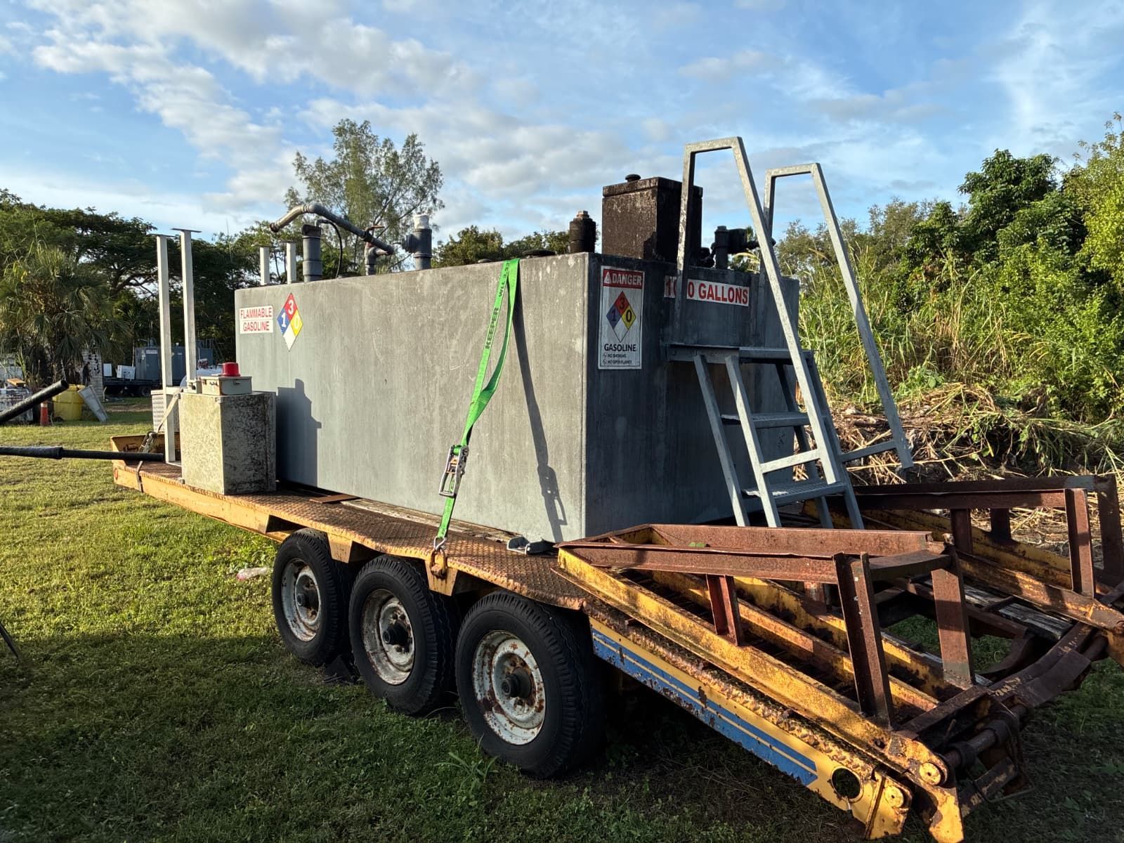A rectangular fuel tank on a rusty trailer. Ladder leads to the top. Green straps secure the tank.