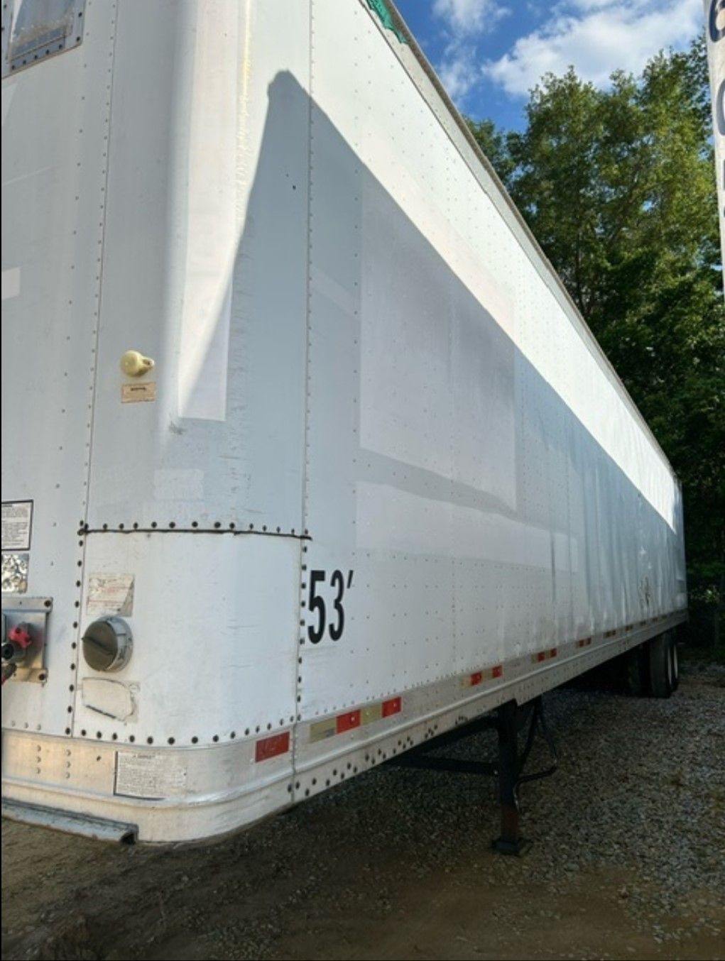 White 53-foot semi-trailer on a gravel lot under a partly cloudy sky. The number 
