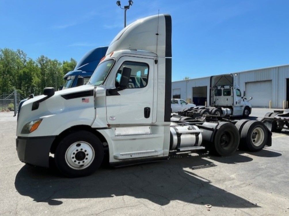 White semi-truck parked outdoors on a sunny day. Another truck is visible in the background.