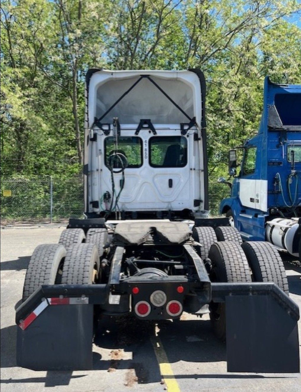 Rear view of a white semi-truck with dual rear wheels and black mud flaps parked outdoors.