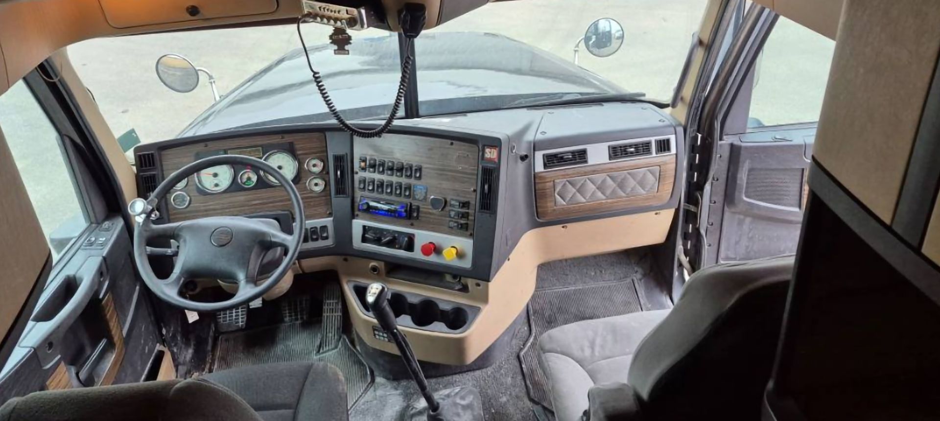 Interior view of a semi-truck cab showing the dashboard, steering wheel, and seats.