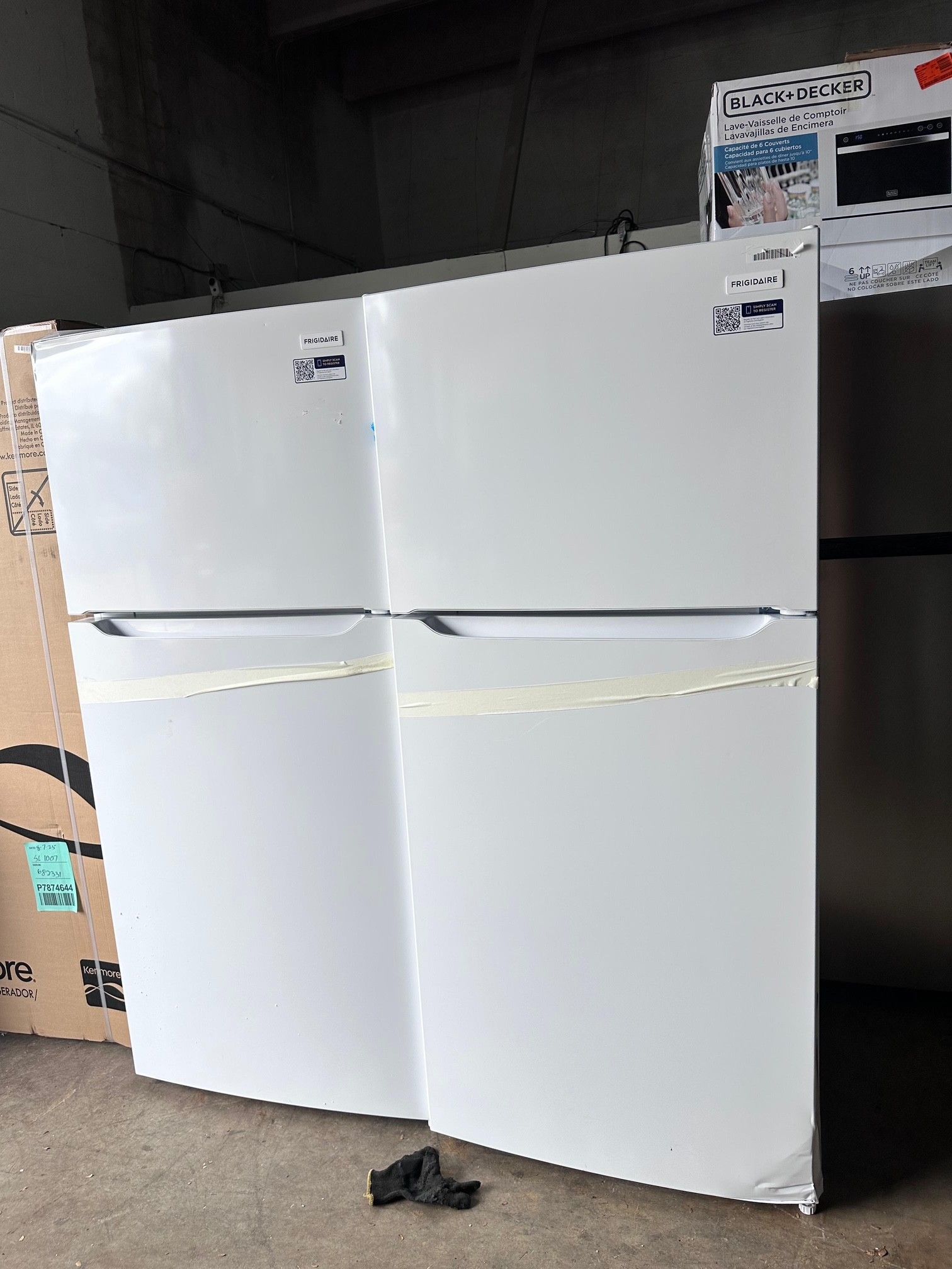 Two white top-freezer refrigerators side-by-side in a warehouse setting.