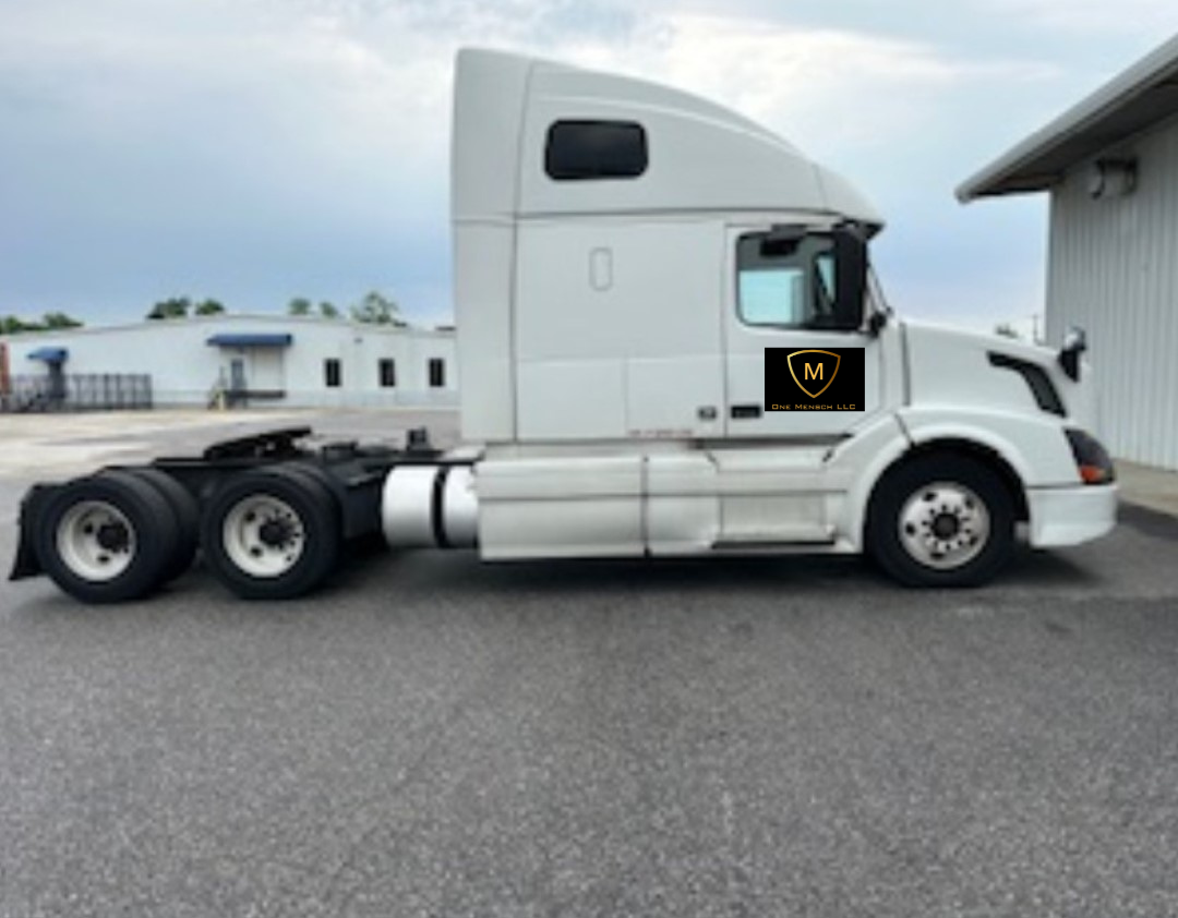 White semi-truck parked outdoors. Shows side profile, cloudy sky, building in background.