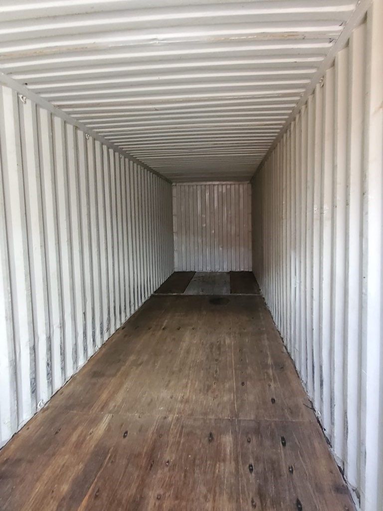 Interior of an empty white shipping container with a wooden floor.
