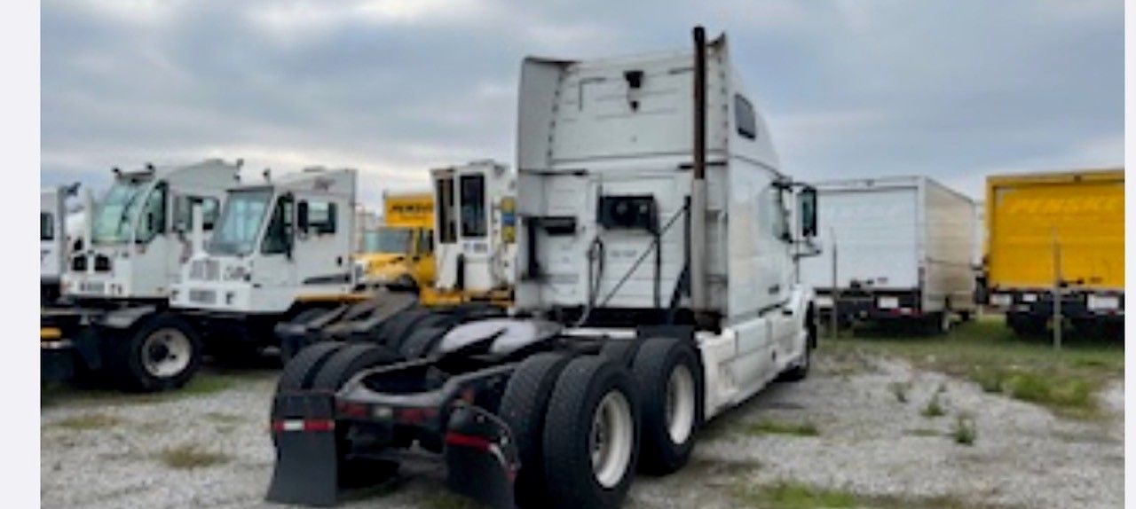 A white semi-truck parked in a lot with other vehicles under a cloudy sky.