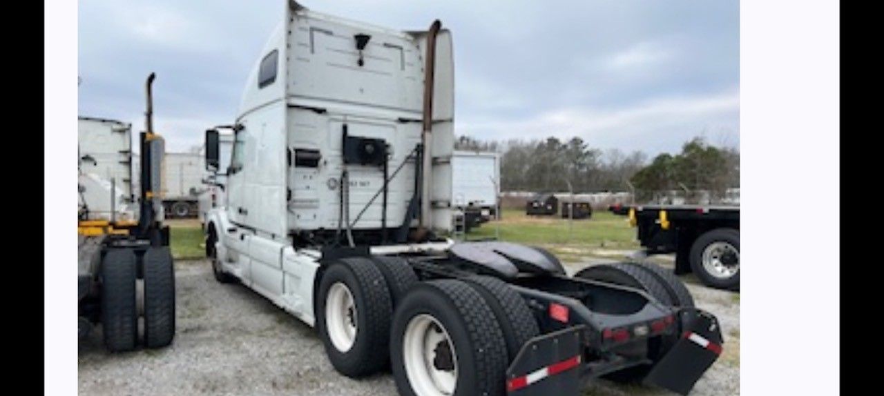 Rear view of a white semi-truck with dual rear wheels parked in a lot under a cloudy sky.