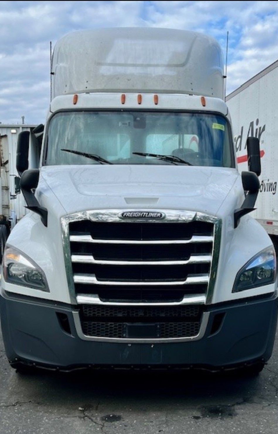 White Freightliner semi-truck parked outdoors, facing the viewer. The grill and headlights are visible, with the cab and mirrors also in view.