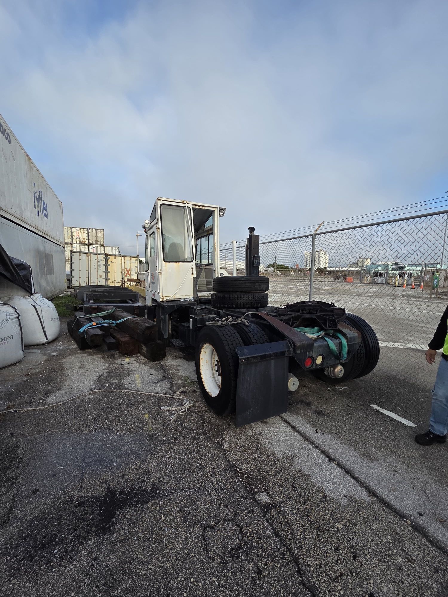 White yard truck parked on asphalt; containers and fence in the background.