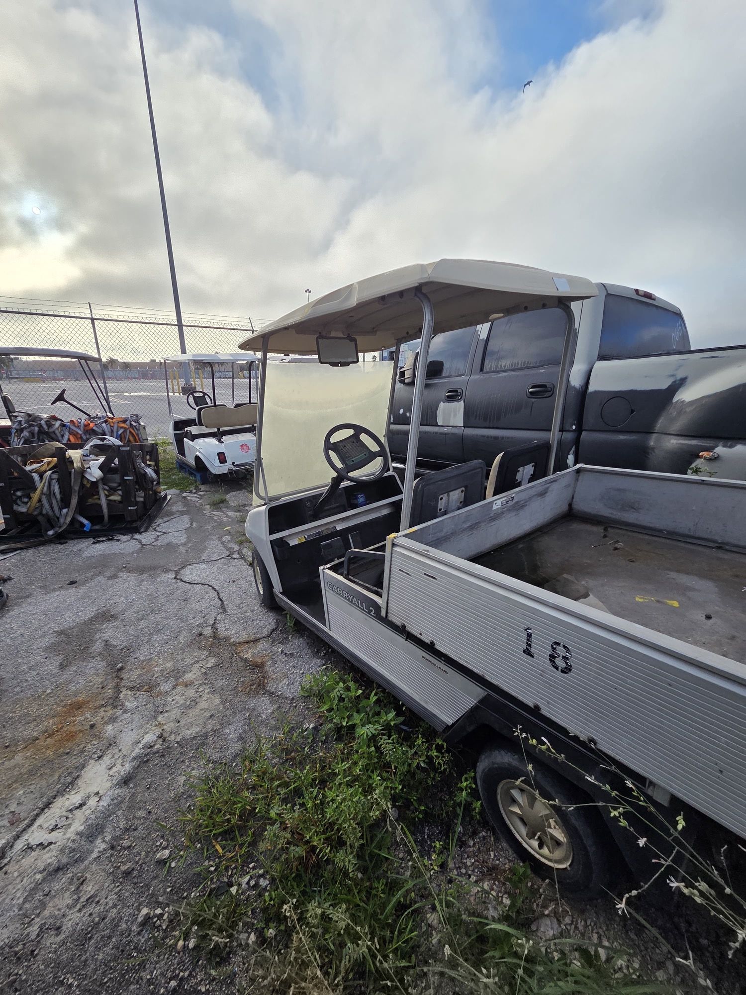 Gray utility golf cart with white canopy parked near a fence, another golf cart visible in the distance.