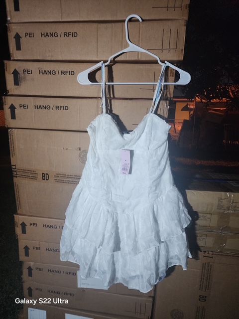White ruffled top on a hanger, in front of a stack of cardboard boxes.