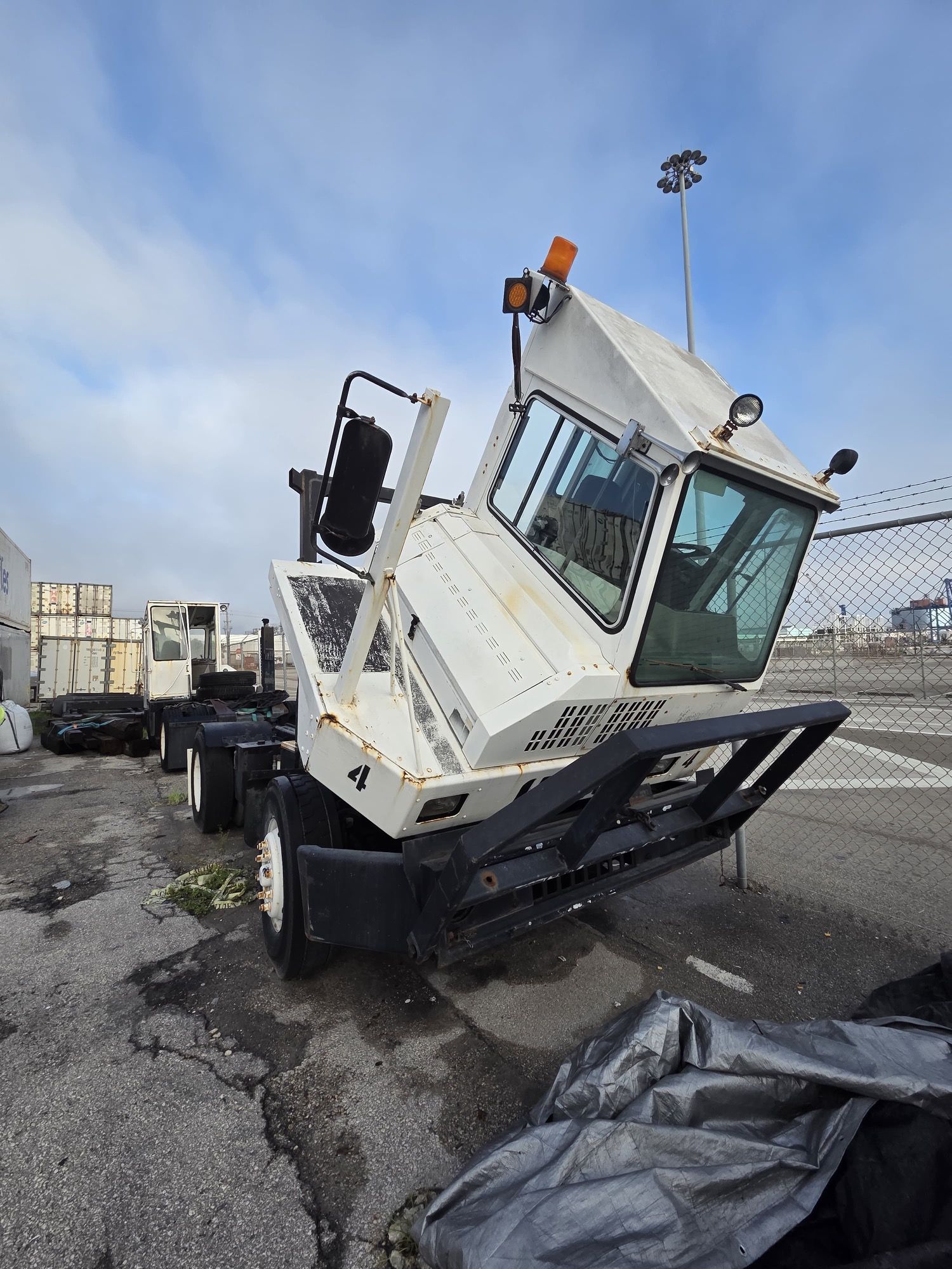 White industrial truck, angled view, with a raised cab, in an outdoor industrial area.