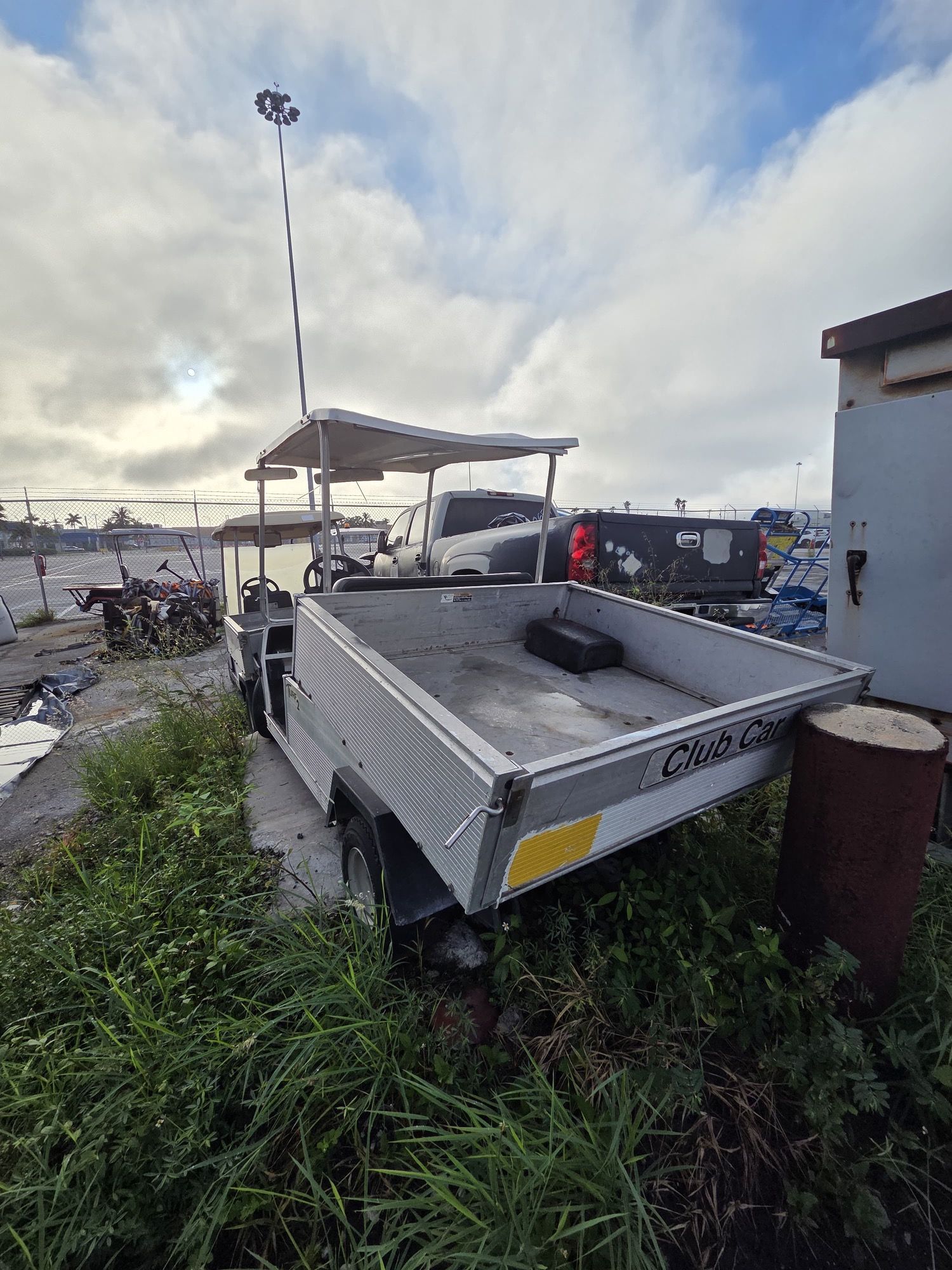 Metal utility cart with canopy, parked on rough ground with grass. Cloudy sky in the background.