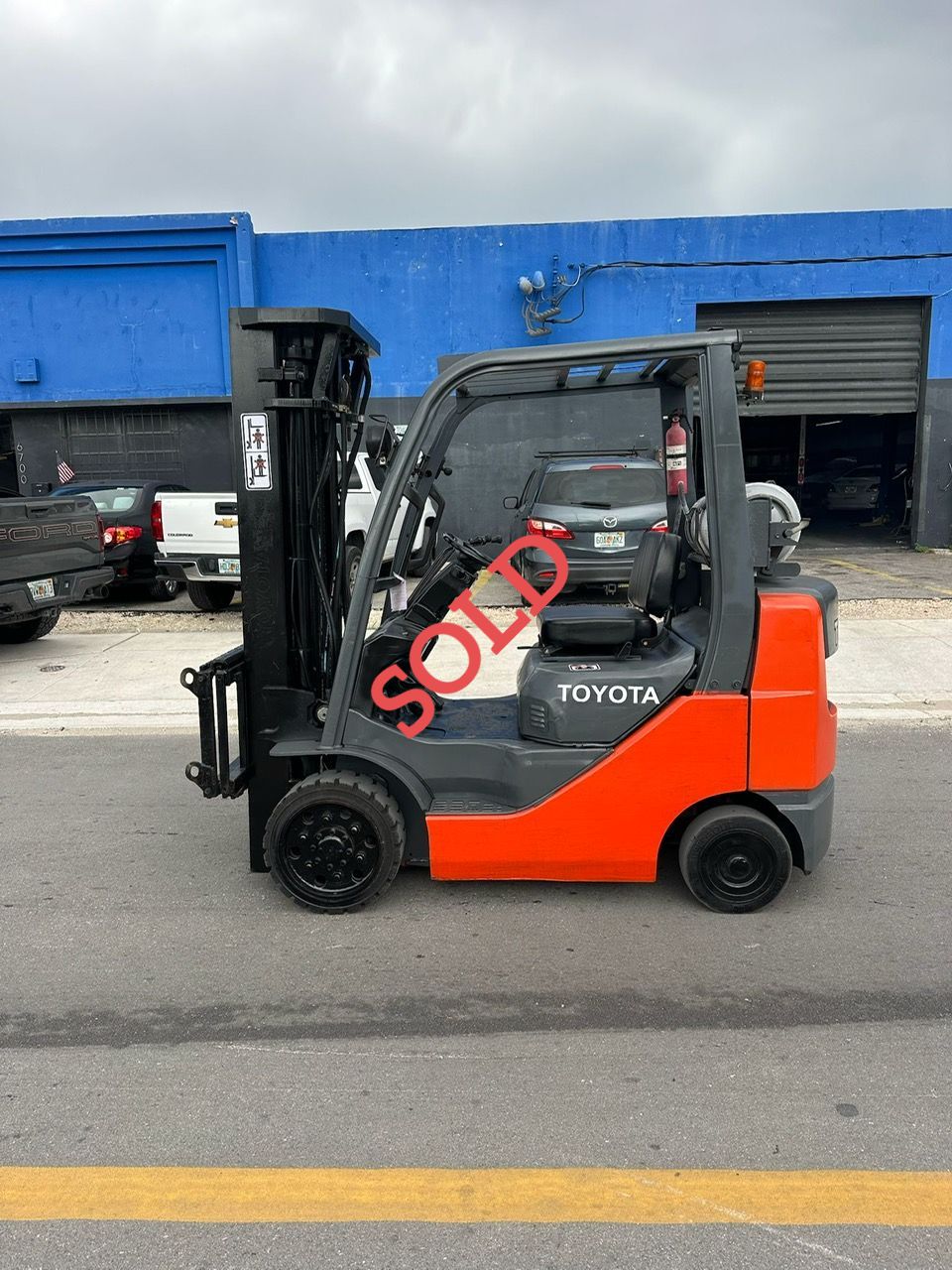 Orange and black Toyota forklift on pavement in front of a blue building with 