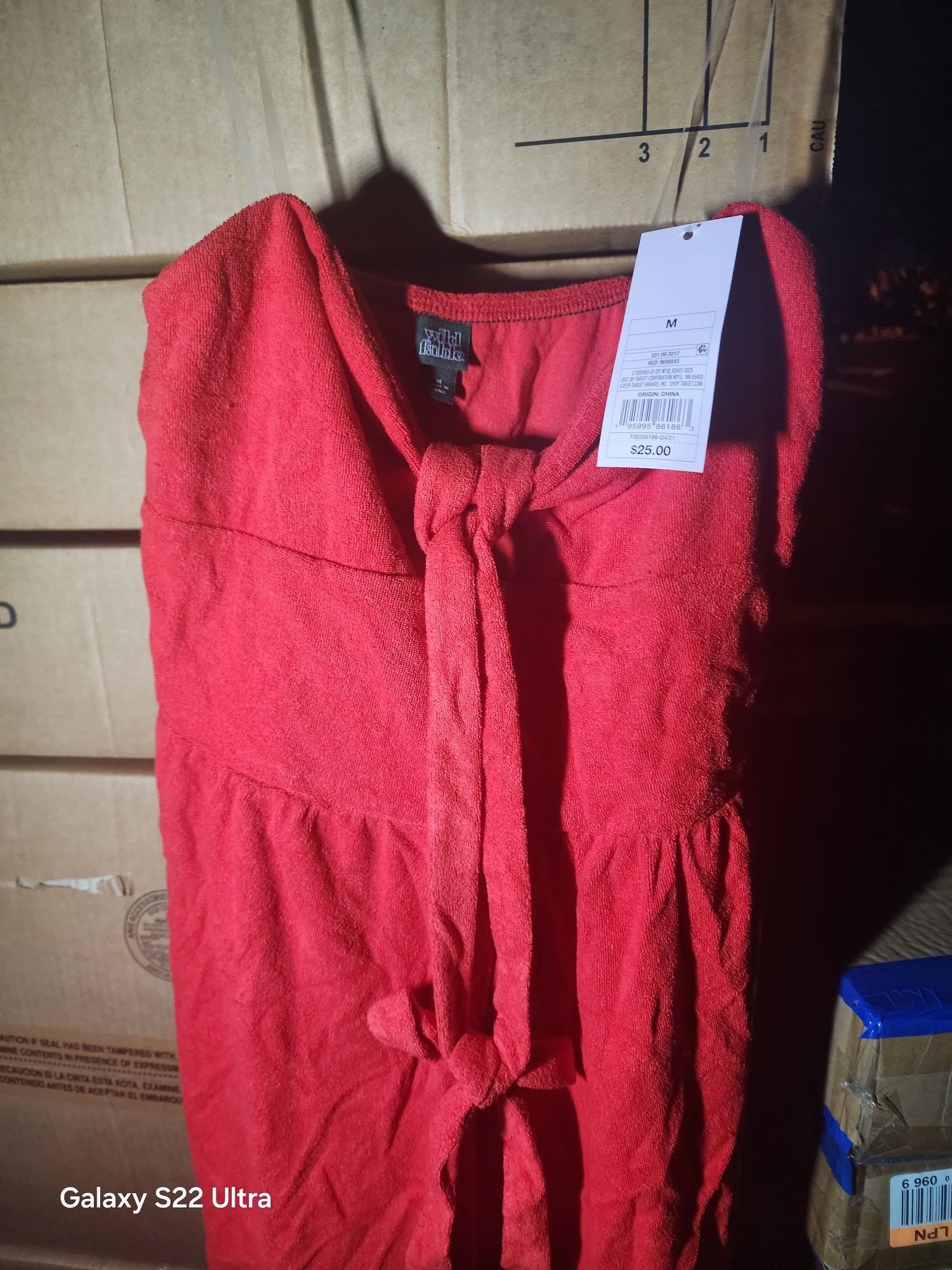 Red textured dress with attached tag, resting on cardboard boxes.