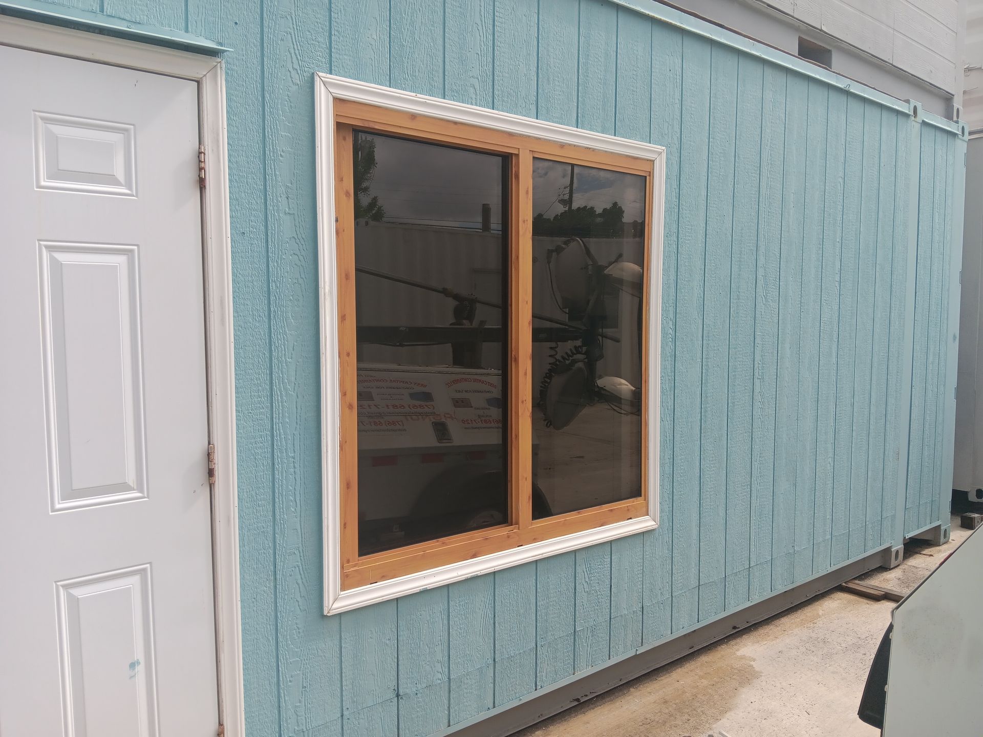 Blue building with a brown-framed window and a white door. The window reflects a blurred outdoor scene.