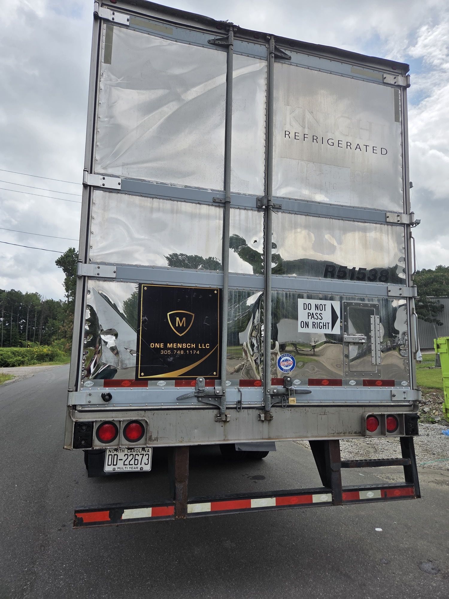 Rear view of a semi-trailer with a reflective silver exterior parked on a road.