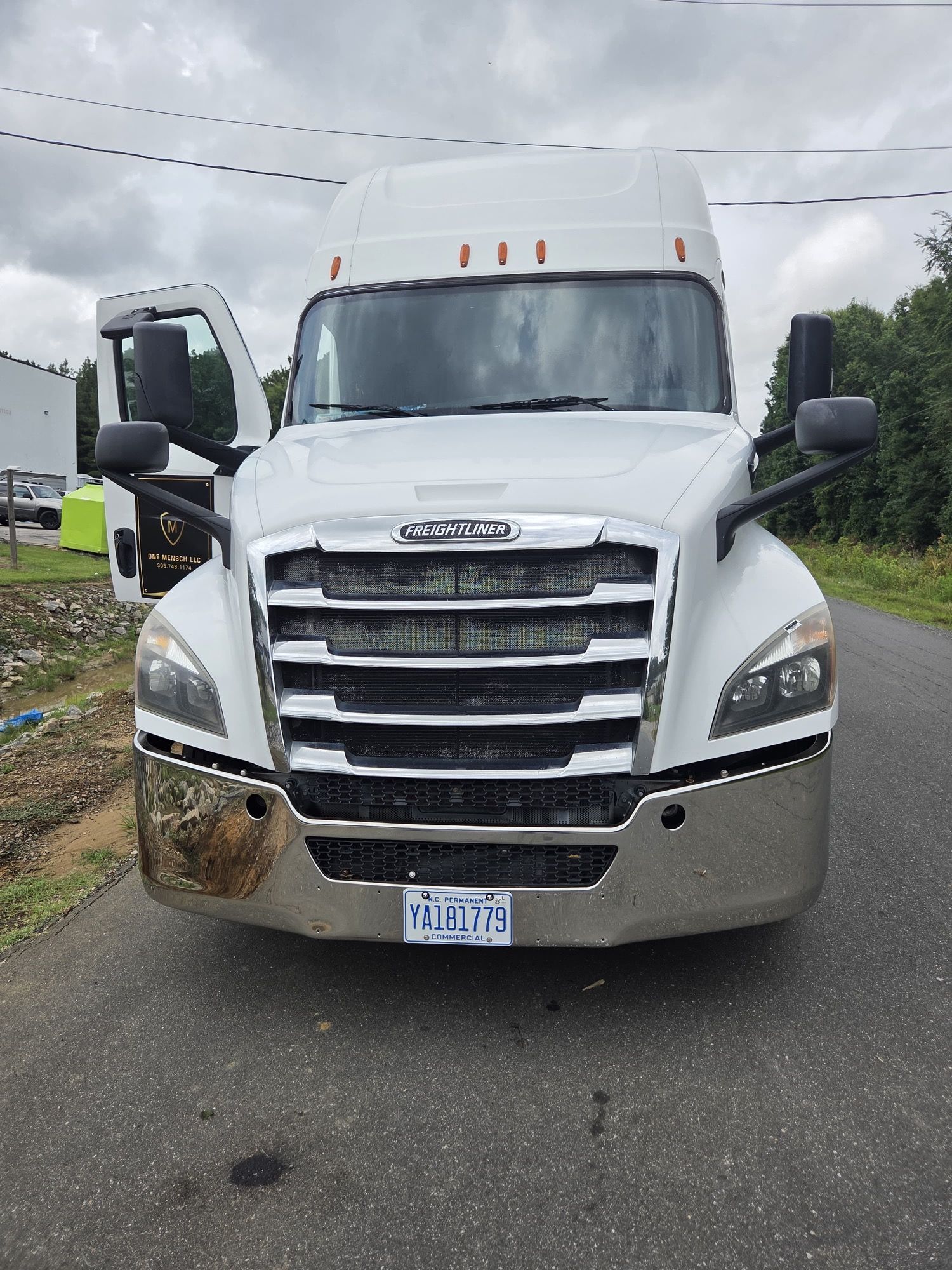 White Freightliner semi-truck parked on road with driver’s door open.