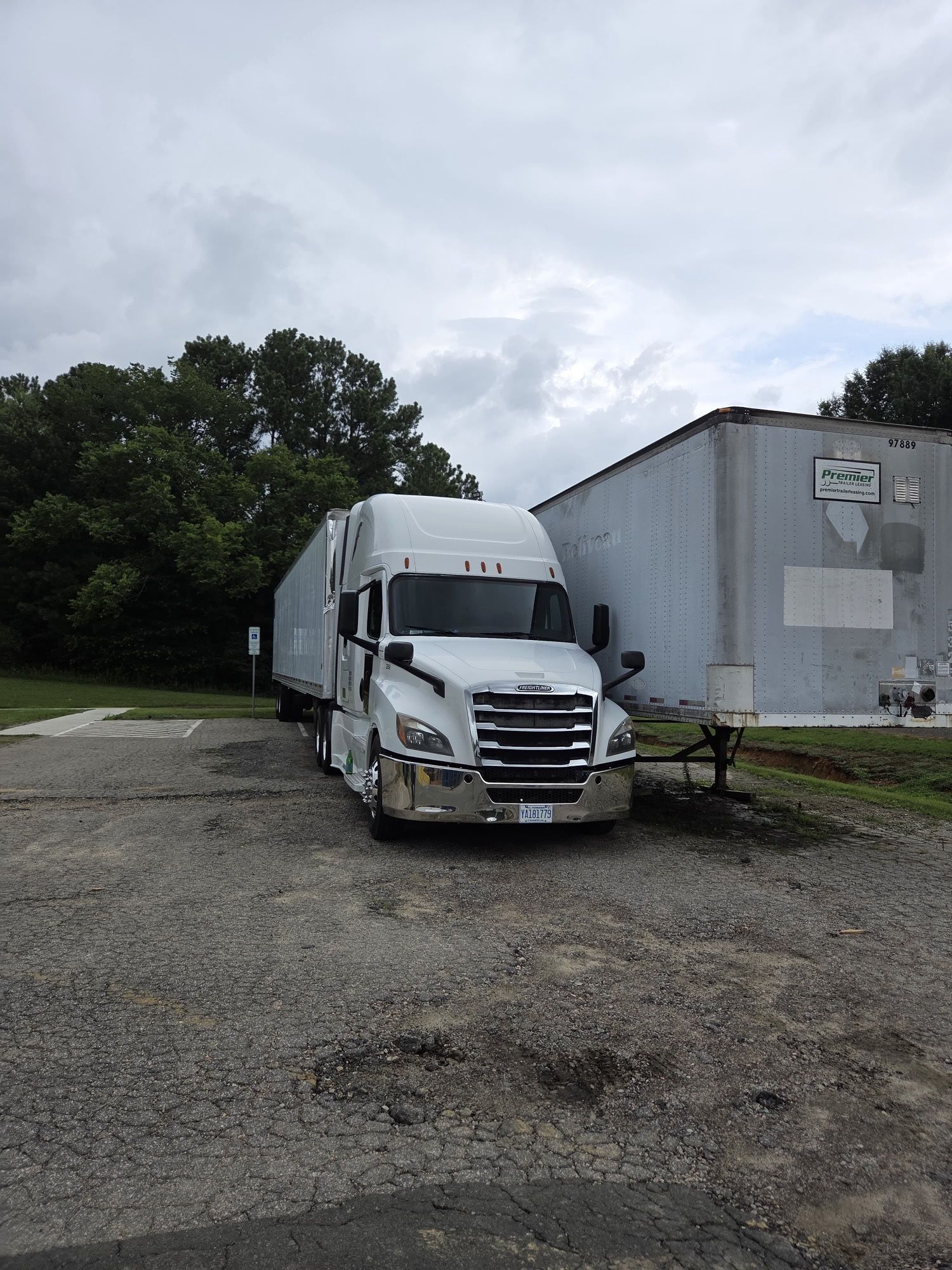 White semi-truck parked on gravel lot beside a plain building, overcast sky.