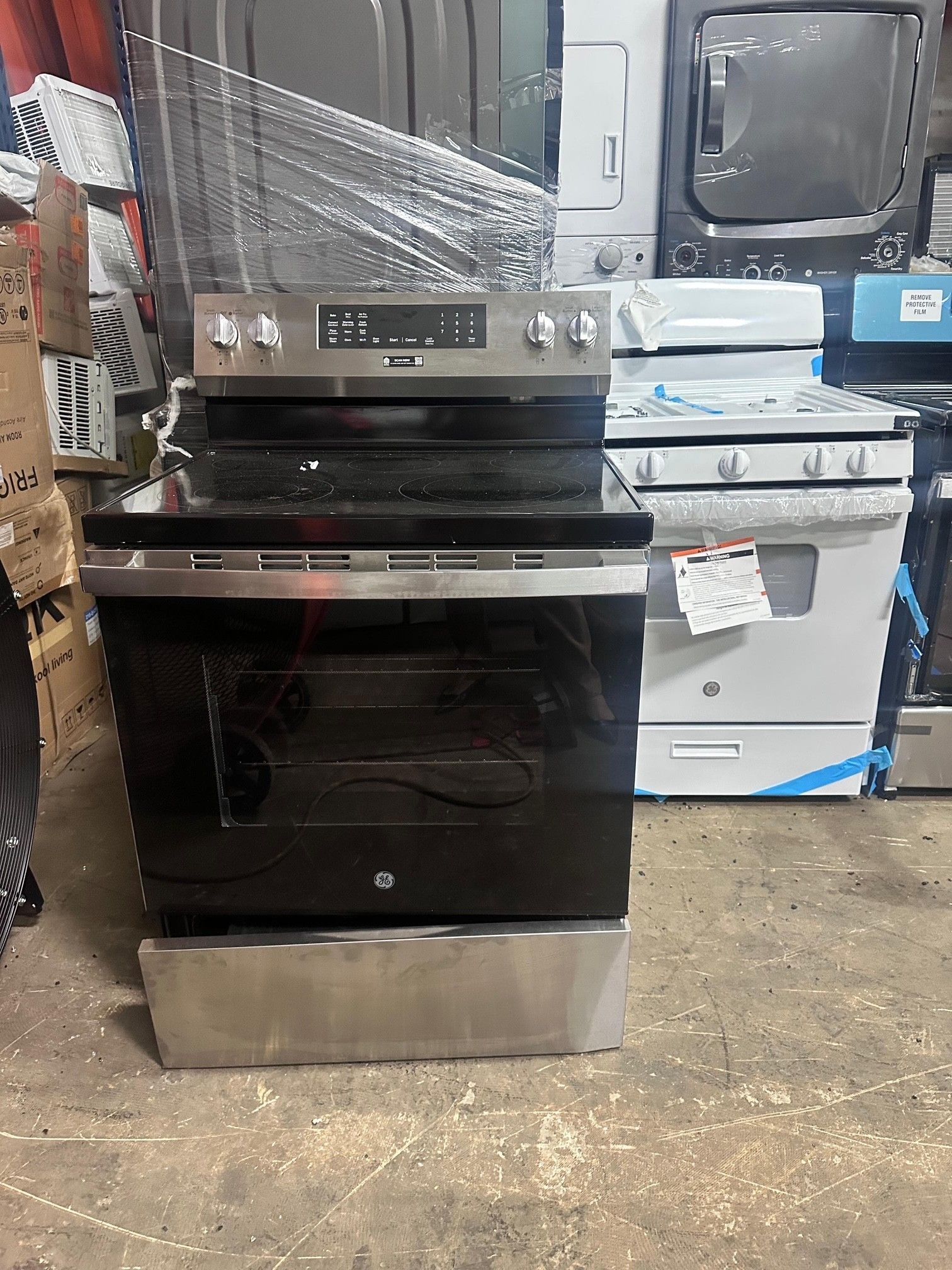 Stainless steel electric range with black cooktop and oven door in a store setting.