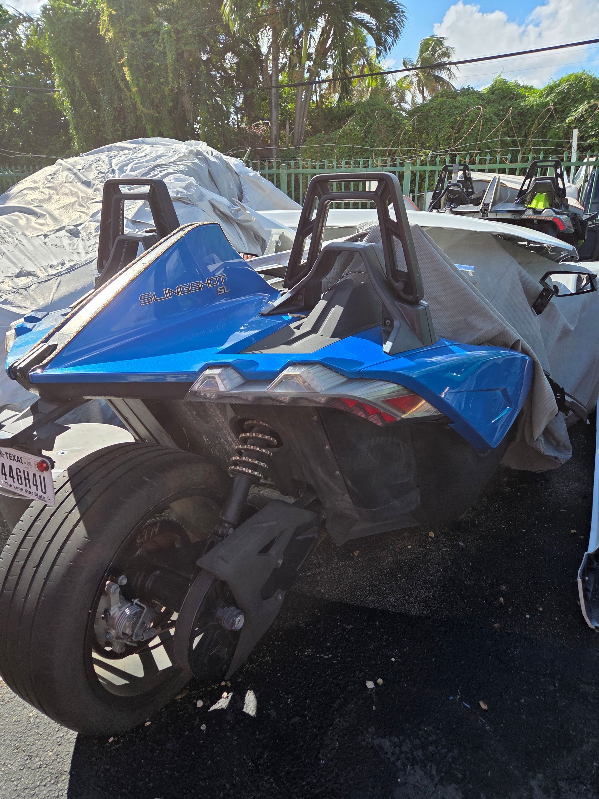 Blue and black Polaris Slingshot partially covered, parked outdoors.