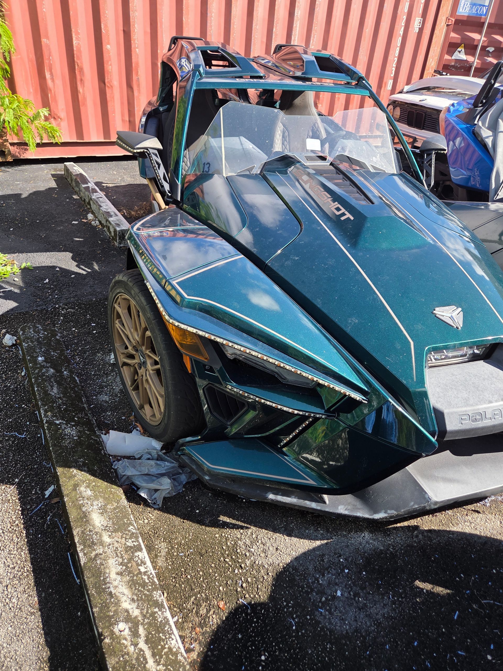 Green Polaris Slingshot three-wheeled vehicle parked, damaged front.