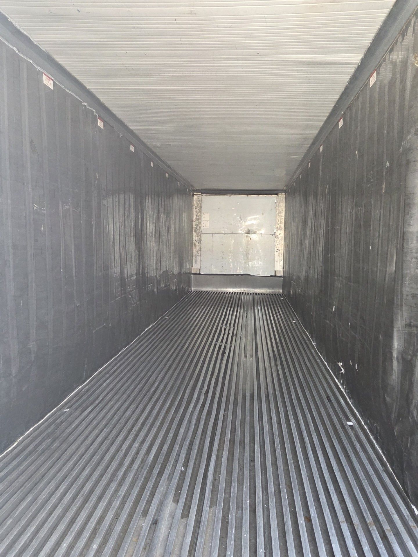 Empty black semi-trailer interior with ribbed floor, dark walls, and a metal door at the end.