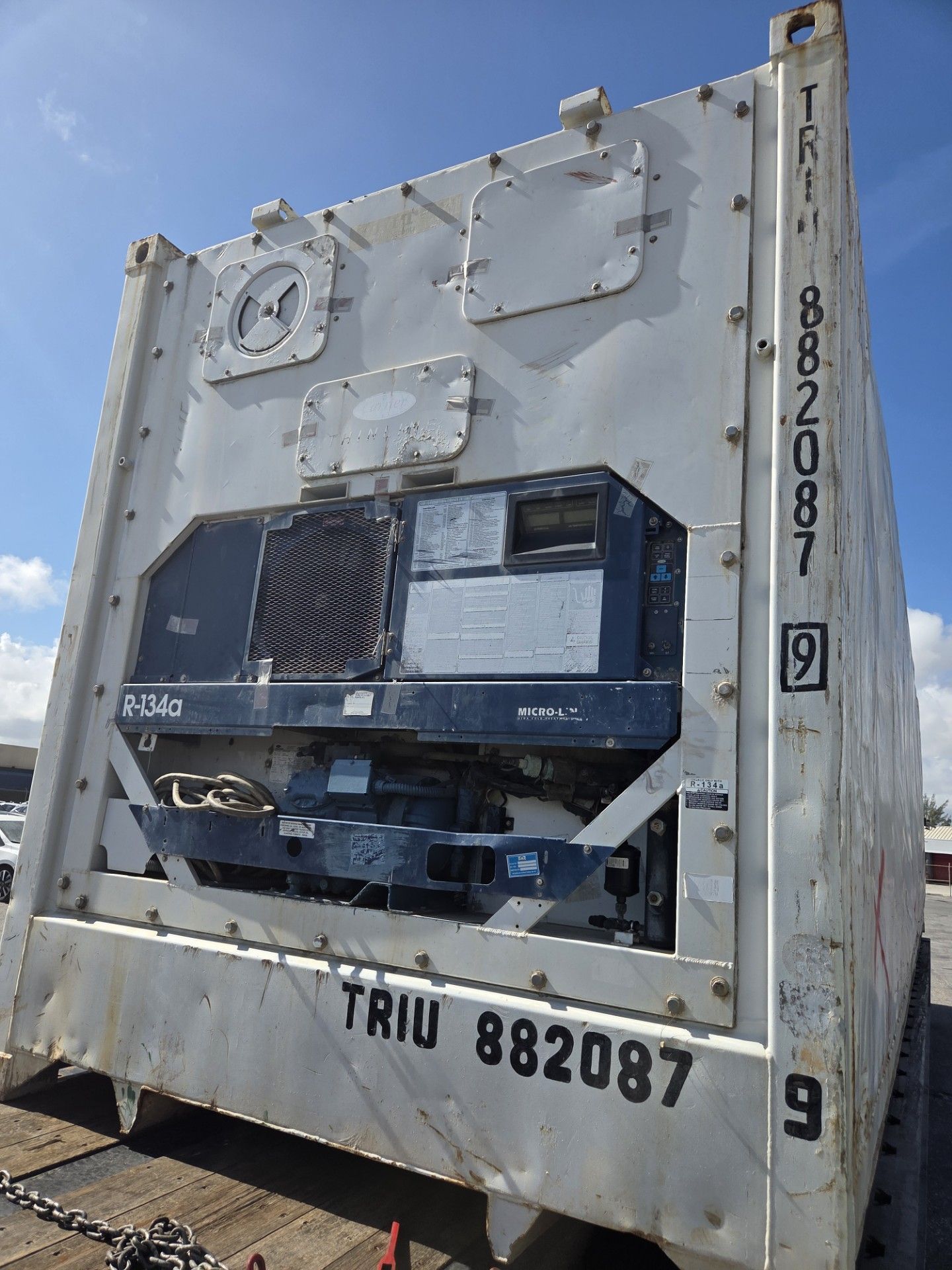 White refrigerated shipping container with black refrigeration unit against a blue sky.