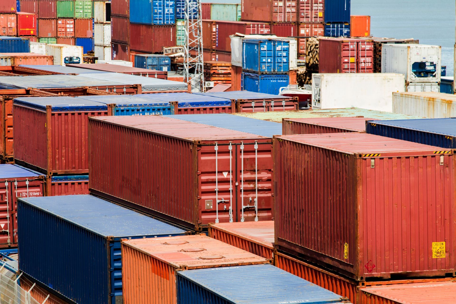 Shipping containers stacked in a port; various colors including red, blue, and white.