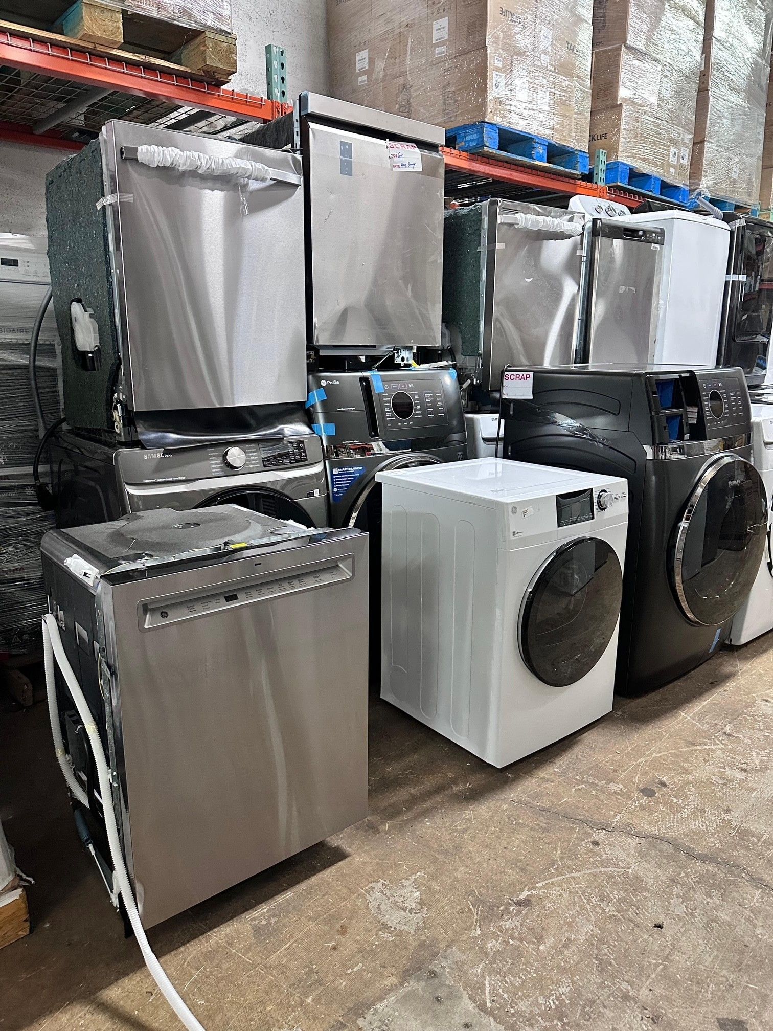 Pile of stainless steel dishwashers and washing machines in a warehouse setting.