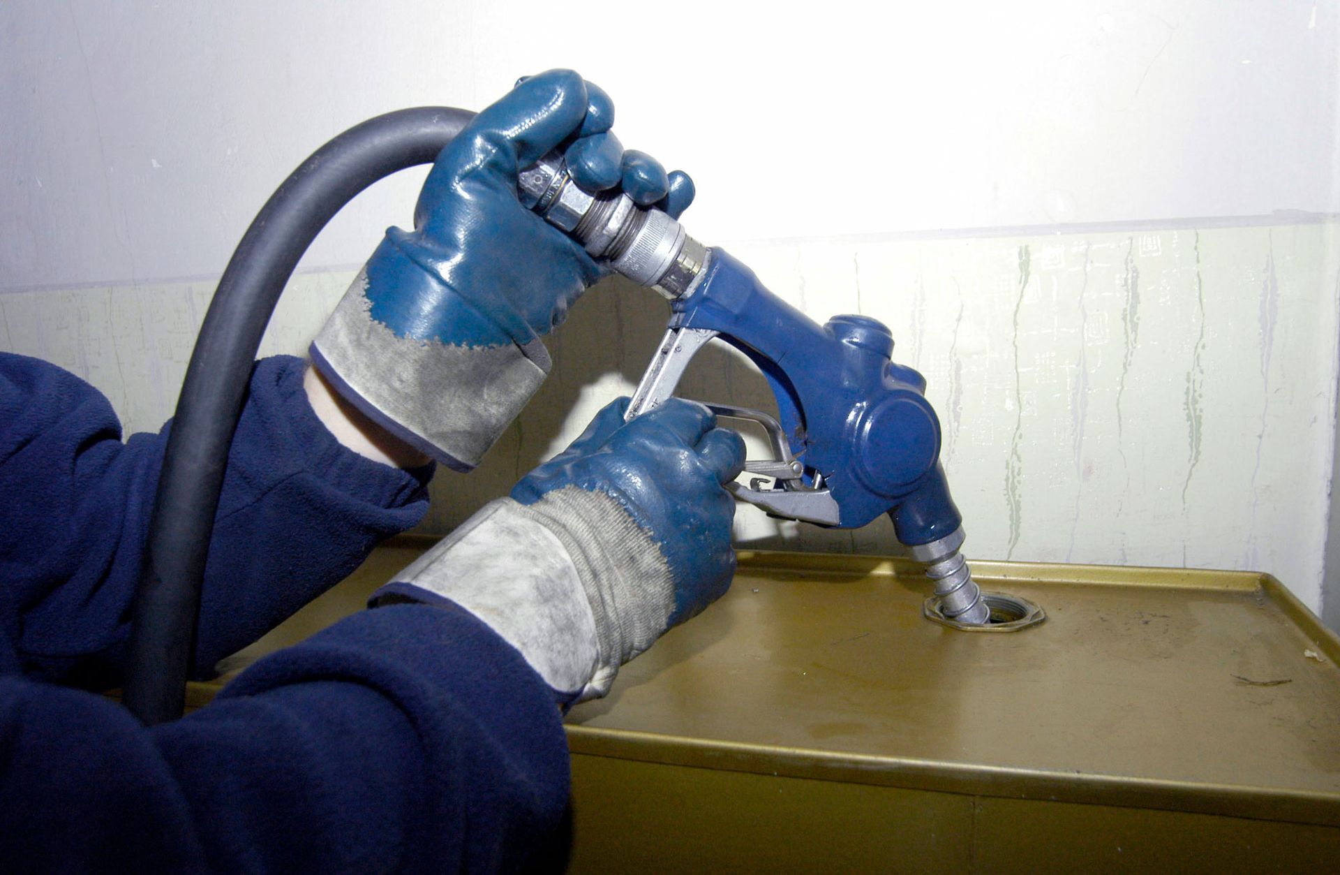 A person wearing blue gloves is pumping gas into a tank