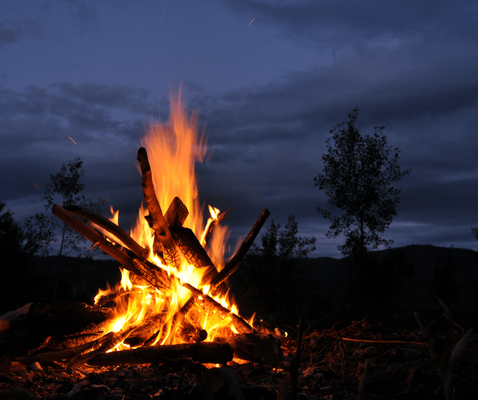 Campfire burning brightly at dusk with dark, cloudy sky.