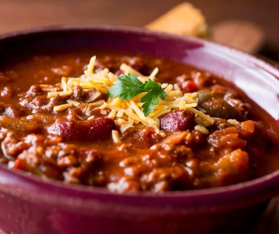 Bowl of chili topped with shredded cheese and parsley garnish.