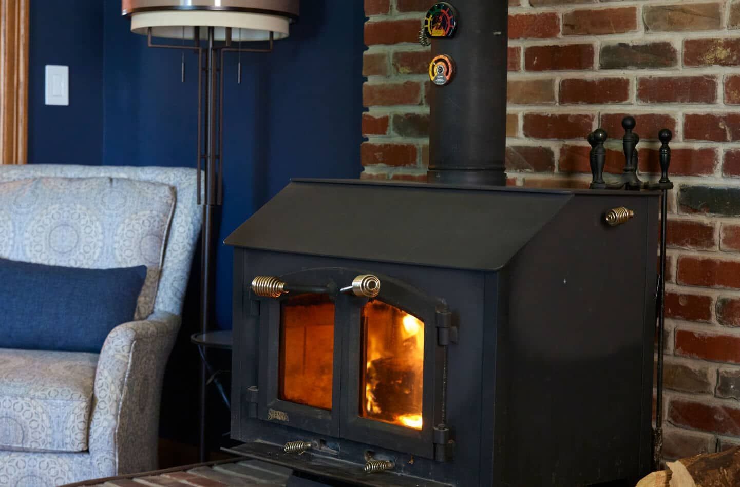 Wood-burning stove with flames in a room with a brick wall and a blue painted wall.