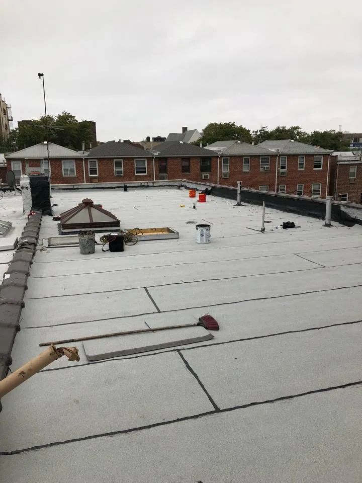 Flat rooftop with white membrane, brick building perimeter, and scattered construction tools under cloudy sky