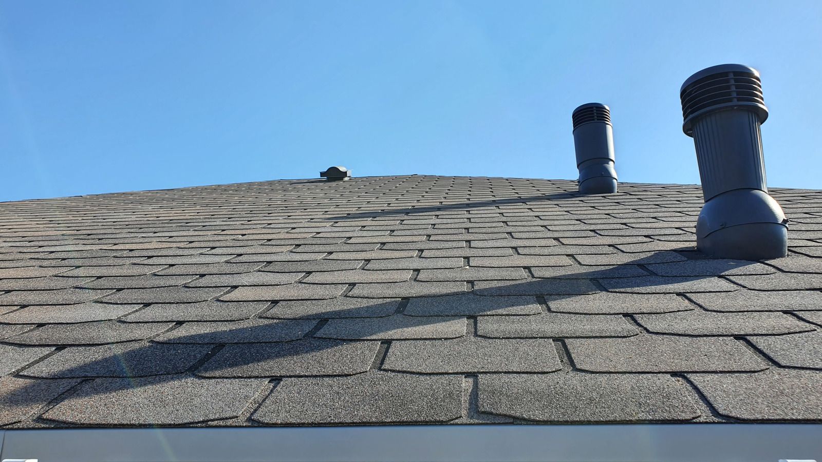 Slate roof with two vent pipes against a clear blue sky