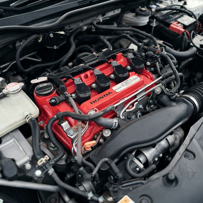Car engine bay with a bright red valve cover and black hoses under the hood