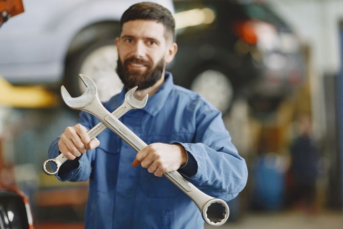 Mechanic in blue coveralls holding two wrenches in an auto repair shop