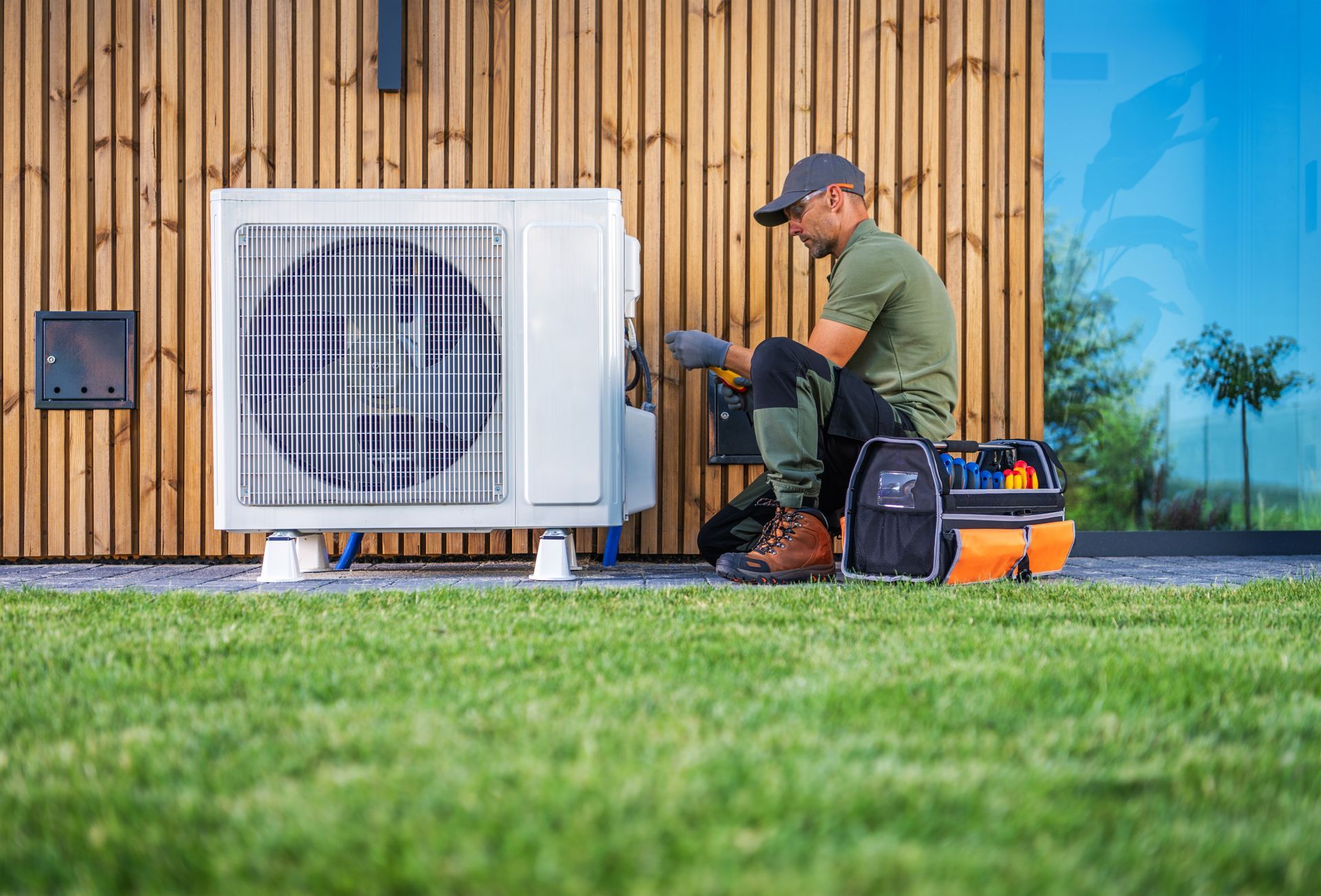 A person installing or repairing an HVAC unit outside a modern building.