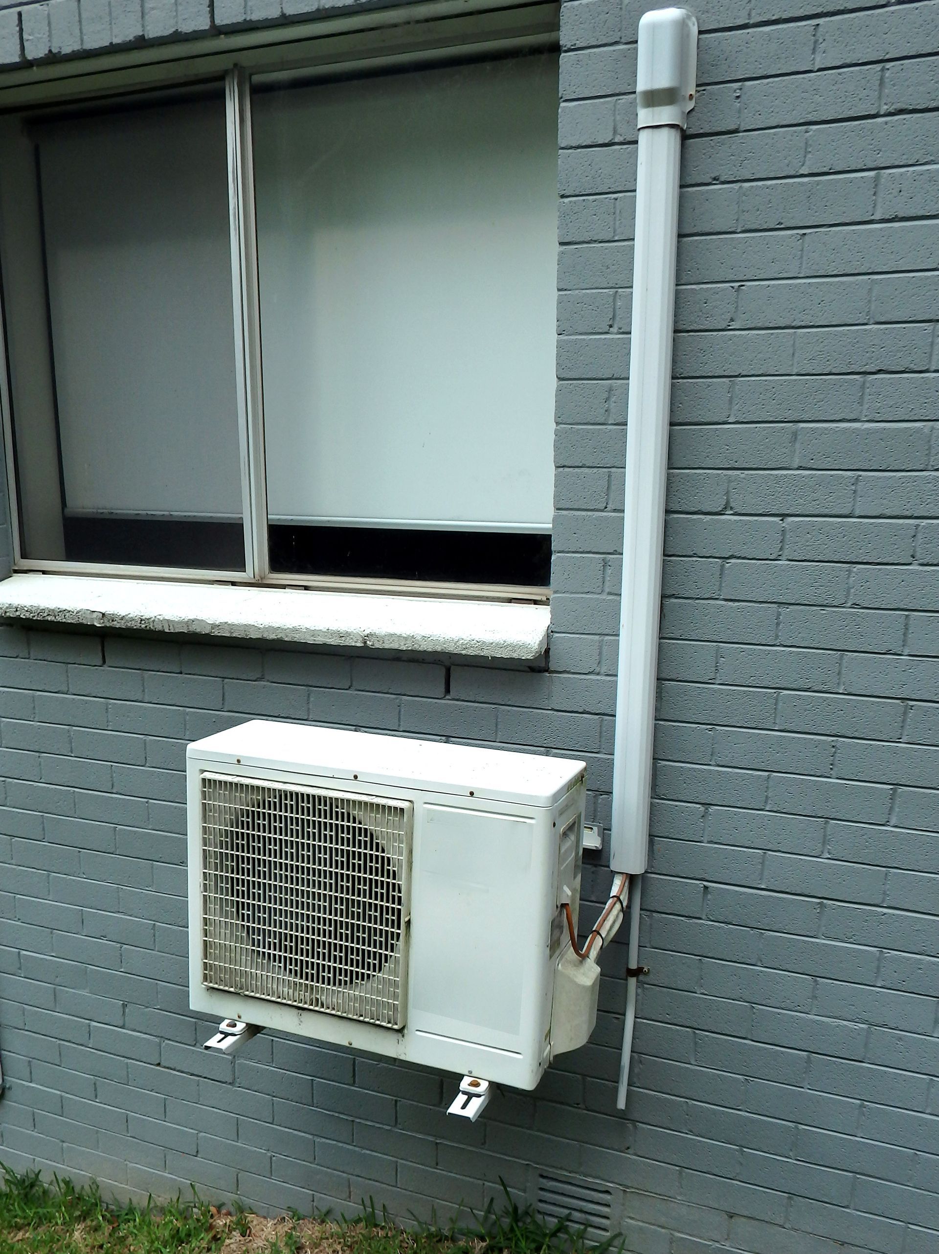 A white air conditioner is mounted on the side of a brick building