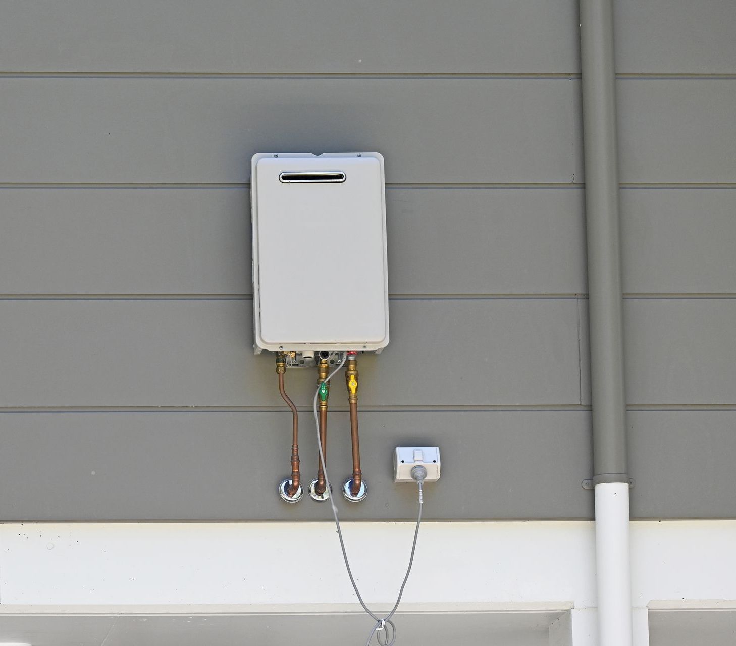 A white water heater is attached to the side of a house.