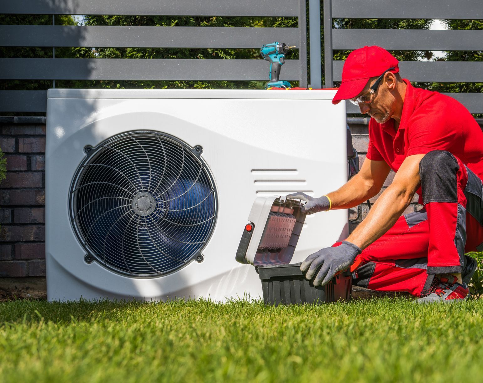A man is working on a heat pump in a backyard.