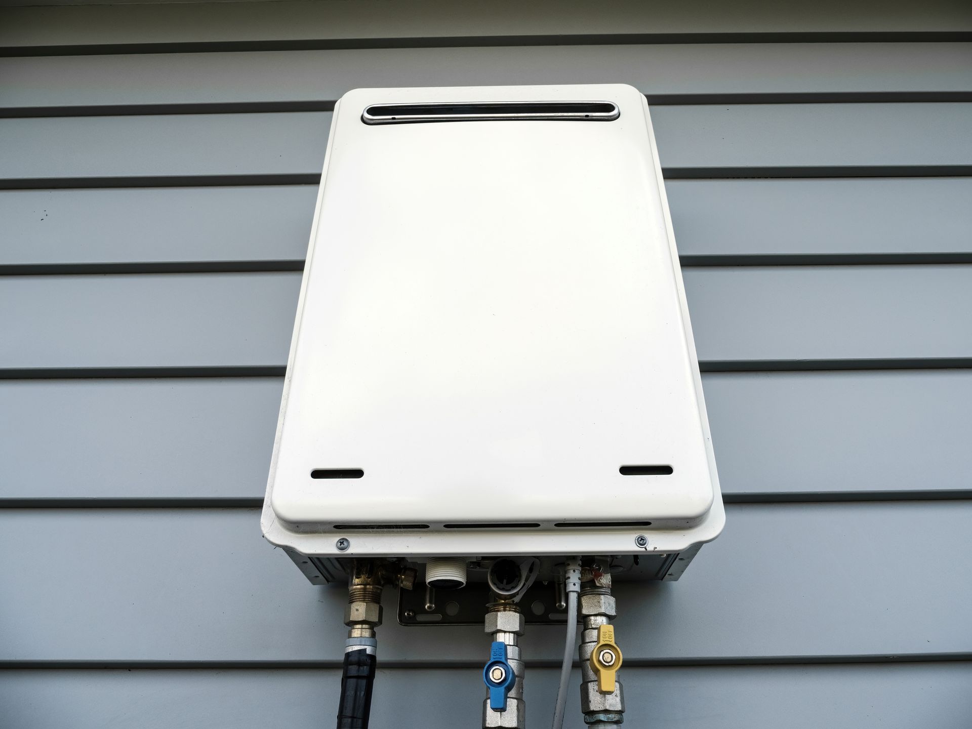 A white water heater is attached to the side of a house.